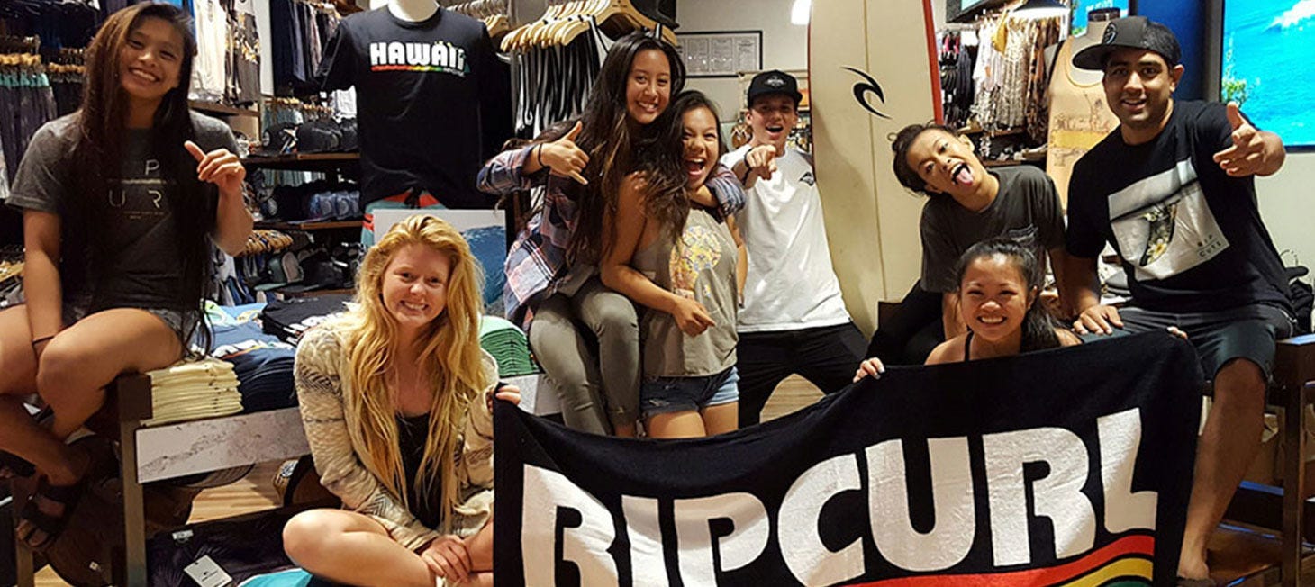Rip Curl Crew posing in their store holding a Rip Curl towel like a banner